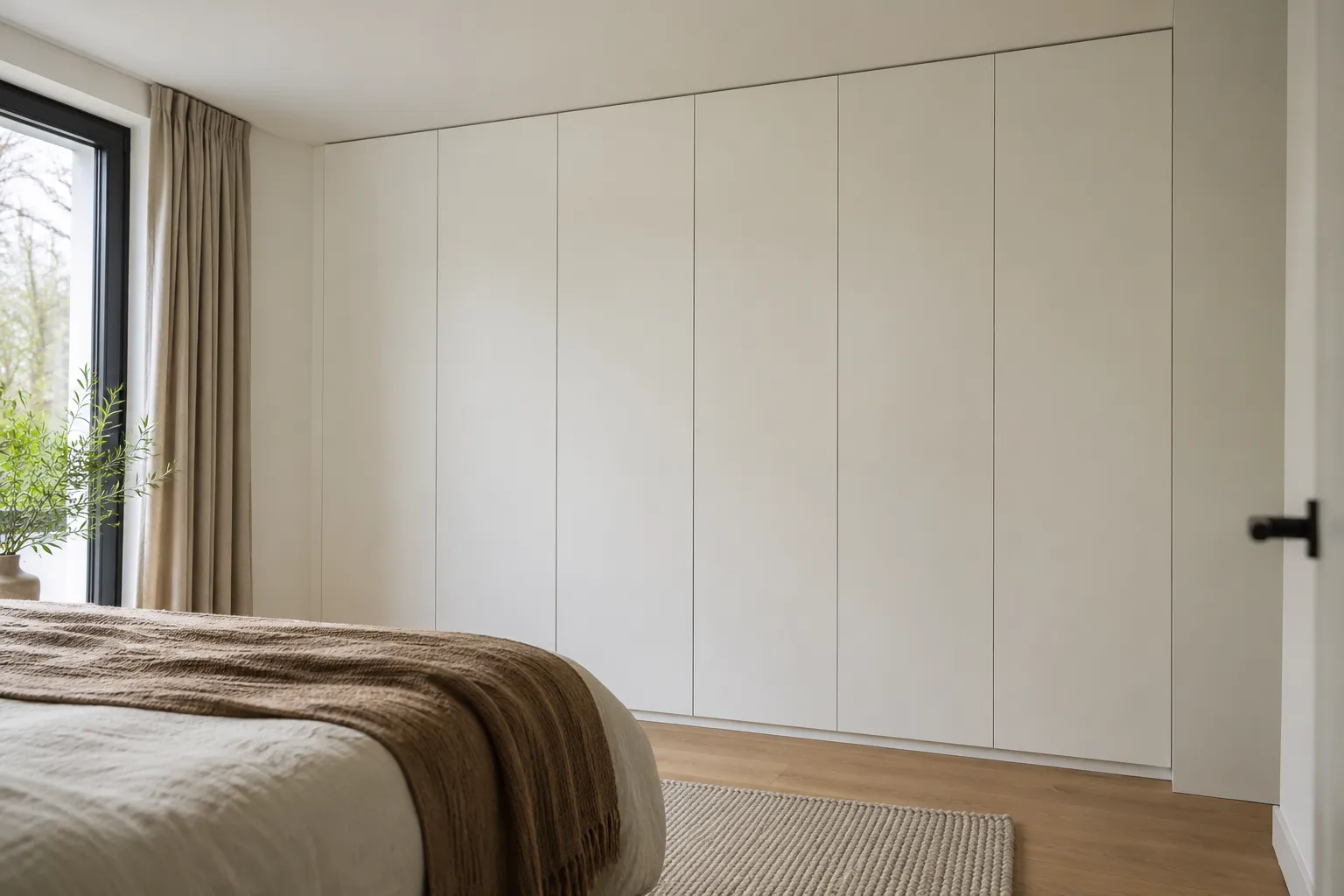 Witte inbouwkast van vloer tot plafond over de hele wand van een slaapkamer, met greeploze deuren